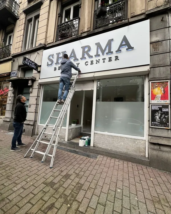 Pose des lettres inox Sharma Beauty Center sur la façade, depuis une échelle